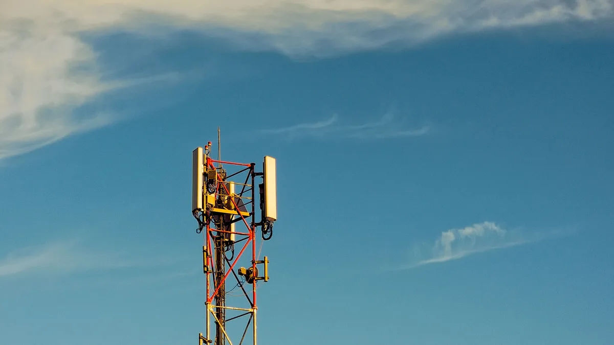 Ein hoher Mobilfunkmast mit Antennen unter einem klaren blauen Himmel mit vereinzelten Wolken.