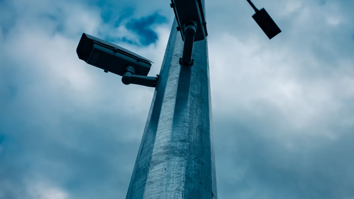 Aufnahme aus niedriger Perspektive von CCTV-Kameras, die an einem hohen Mast gegen einen bewölkten Himmel montiert sind.