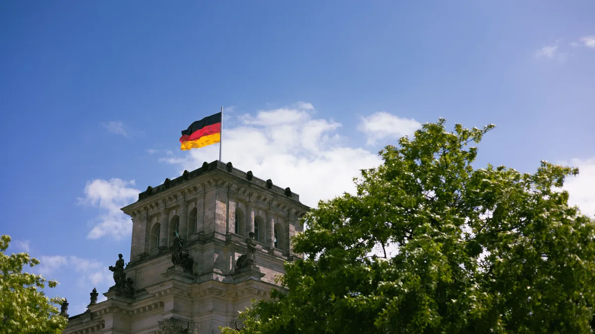 Der ikonische Reichstag in Berlin mit der hoch wehenden deutschen Flagge vor einem klaren blauen Himmel.