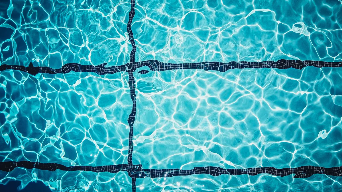 Nahaufnahme einer schimmernden türkisfarbenen Schwimmbadoberfläche mit Fliesenlinien.