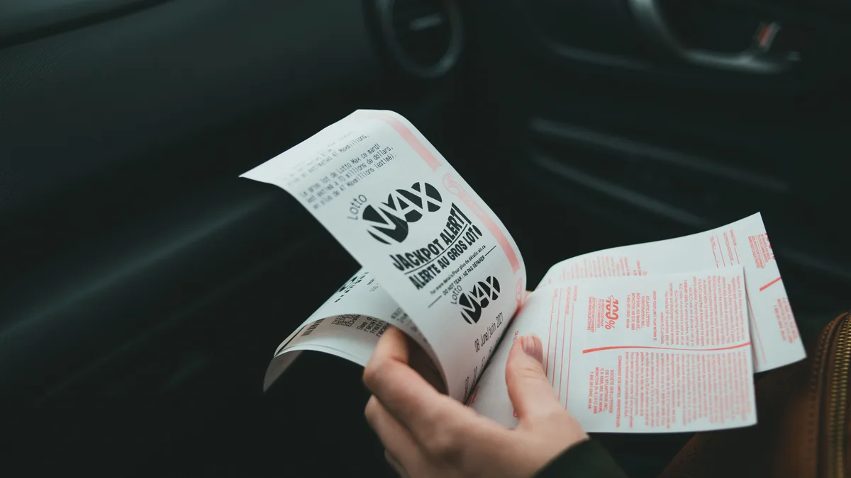 Nahaufnahme von Händen, die Lotto Max-Papiere im Auto halten, was Glück und Zufall symbolisiert.