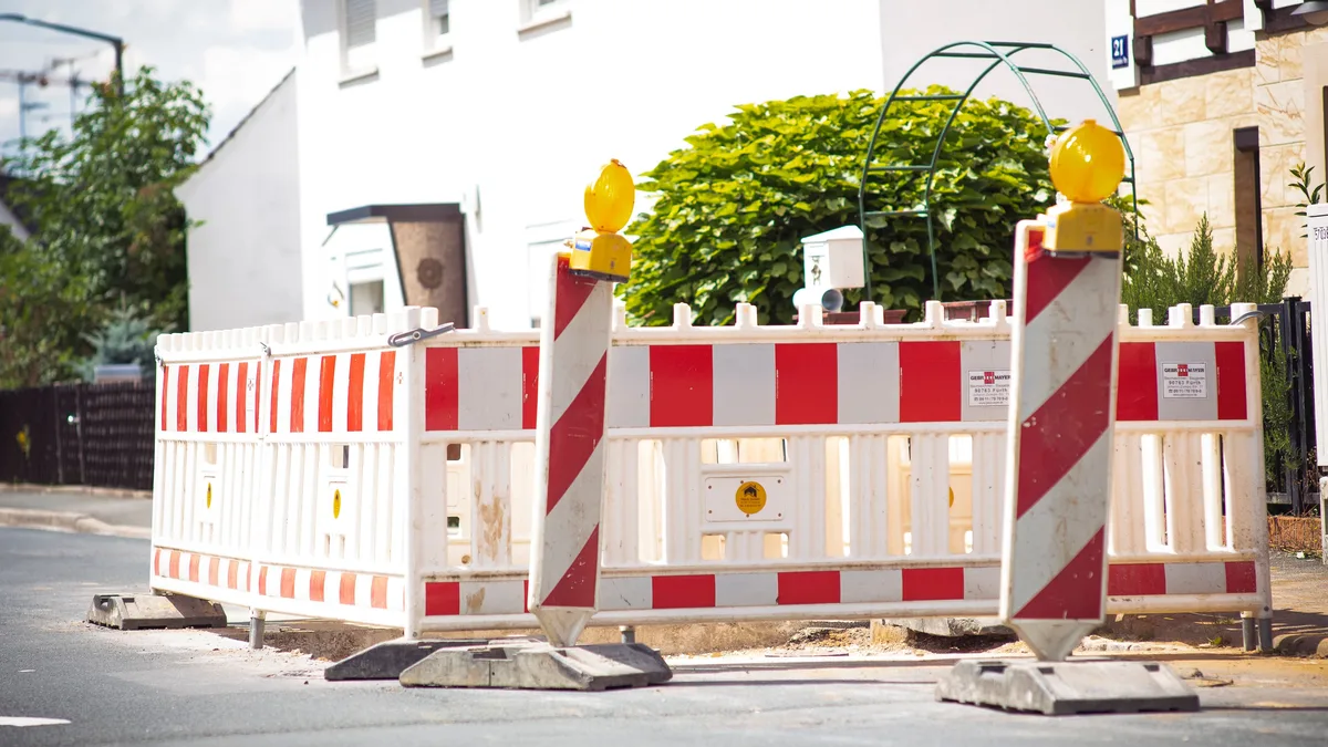 Helle Straßenbarriere mit gestreiftem Muster signalisiert Bauarbeiten in einer Vorstadtstraße.