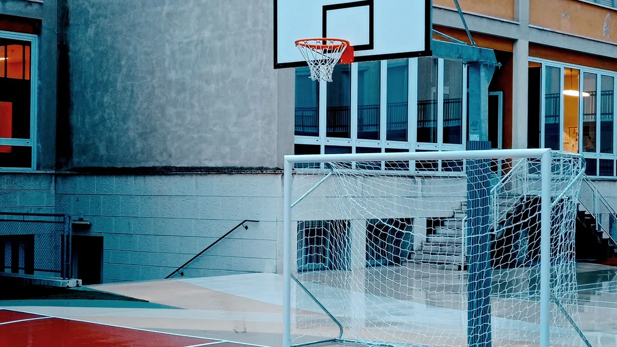 Ein nasser Basketballplatz neben einem Schulgebäude in Verona, Italien, tagsüber.
