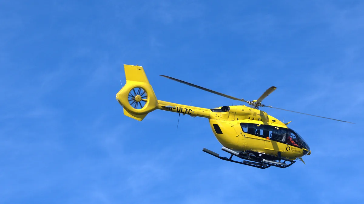 Ein leuchtend gelber Hubschrauber im Flug vor klarem, blauem Himmel.