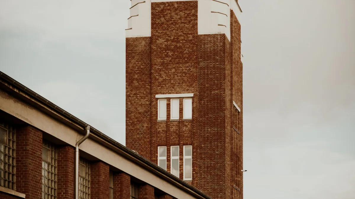 Ein klassischer Uhrenturm aus Backstein steht hoch in einem Industriegebiet unter einem warmen Himmel.