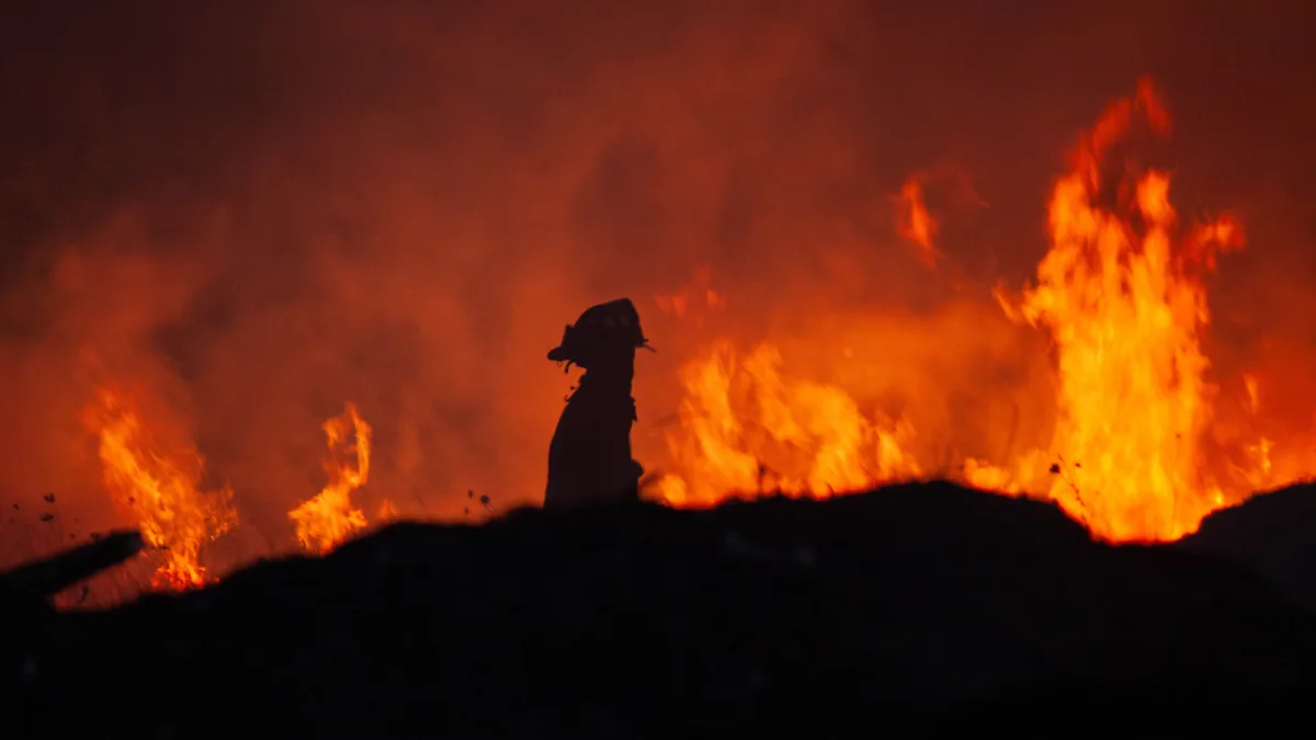 Eine dramatische Silhouette eines Feuerwehrmanns vor einem lodernden Feuer in der Nacht, die Mut und Action betont.