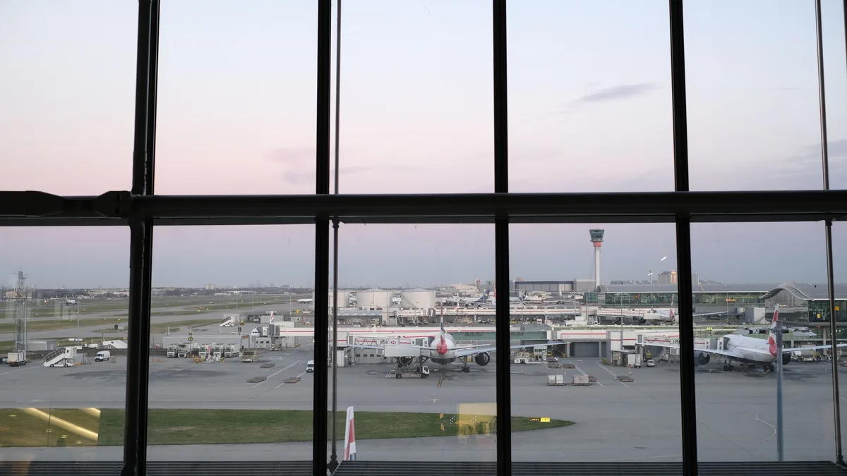 Blick auf das Rollfeld des Flughafens Heathrow und Flugzeuge durch das Terminalfenster während der Dämmerung.