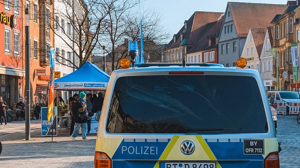 Ein Polizeiwagen, der auf einem lebhaften Platz mit Kopfsteinpflaster und bunten Gebäuden geparkt ist.