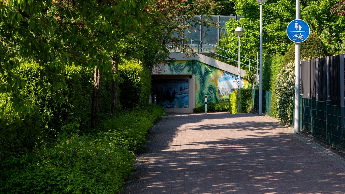 Ein ruhiger Gehweg im Freien, gesäumt von Bäumen und einem Fahrradweg-Schild im Sommer.