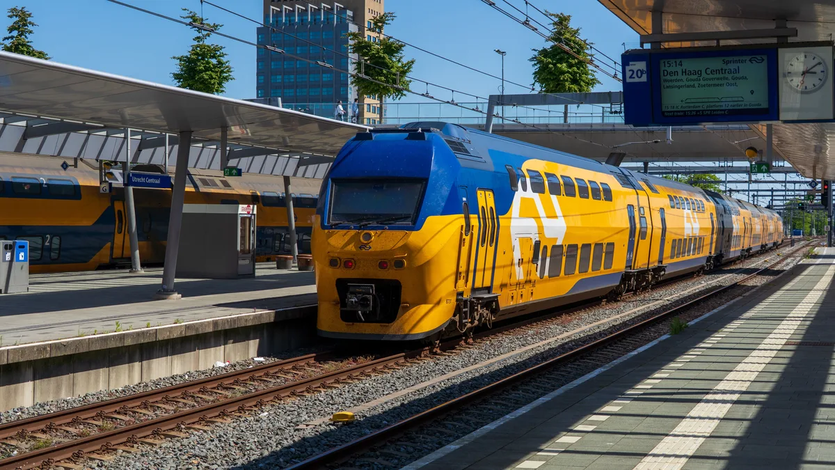 Bunter blauer und gelber Zug, der an einem sonnigen Tag am Utrecht Hauptbahnhof in den Niederlanden ankommt.