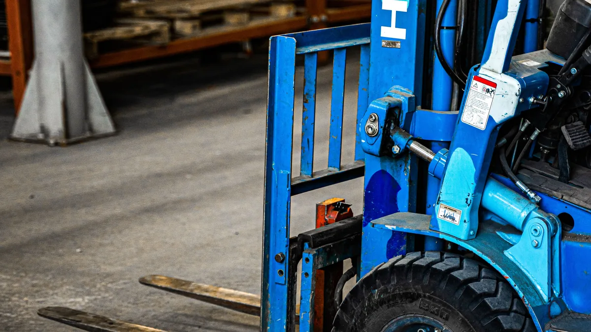 Blauer Gabelstapler in einem Industrie-Lager, geparkt in der Nähe von Regalen mit verschiedenen Gegenständen.