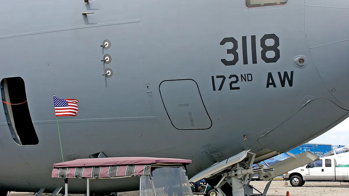 Nahaufnahme eines Militärflugzeugs vom Typ C-17 Globemaster III, das auf einem Flugplatz geparkt ist, in der Nähe steht ein Golfwagen.