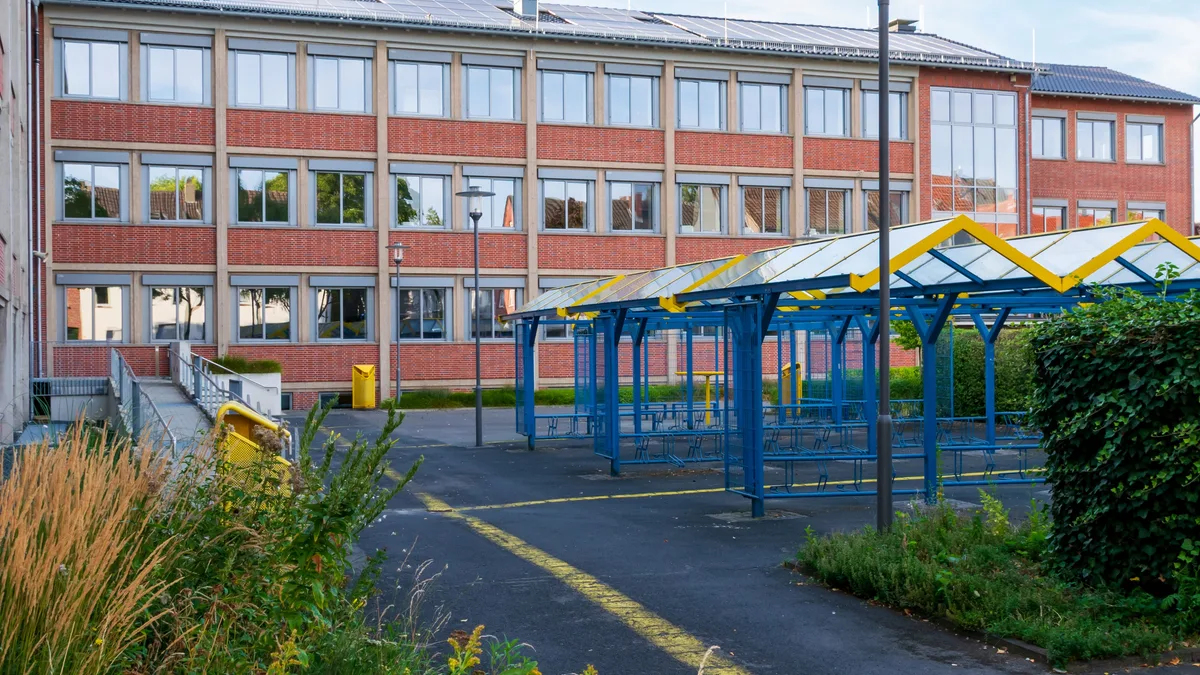 Ein zeitgemäßes Schulgebäude mit bunten Spielplatzstrukturen an einem sonnigen Tag.