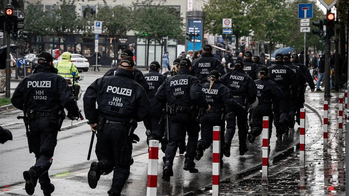 Polizisten, die eine regnerische Straße in Hamburg, Deutschland, hinunterlaufen und die Durchsetzung des Rechts in Aktion zeigen.