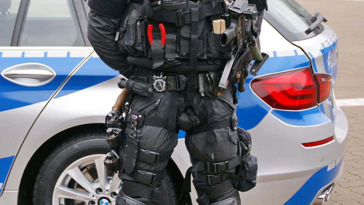 Ein deutscher Polizeibeamter in taktischer Ausrüstung steht vor einem Polizeiauto.