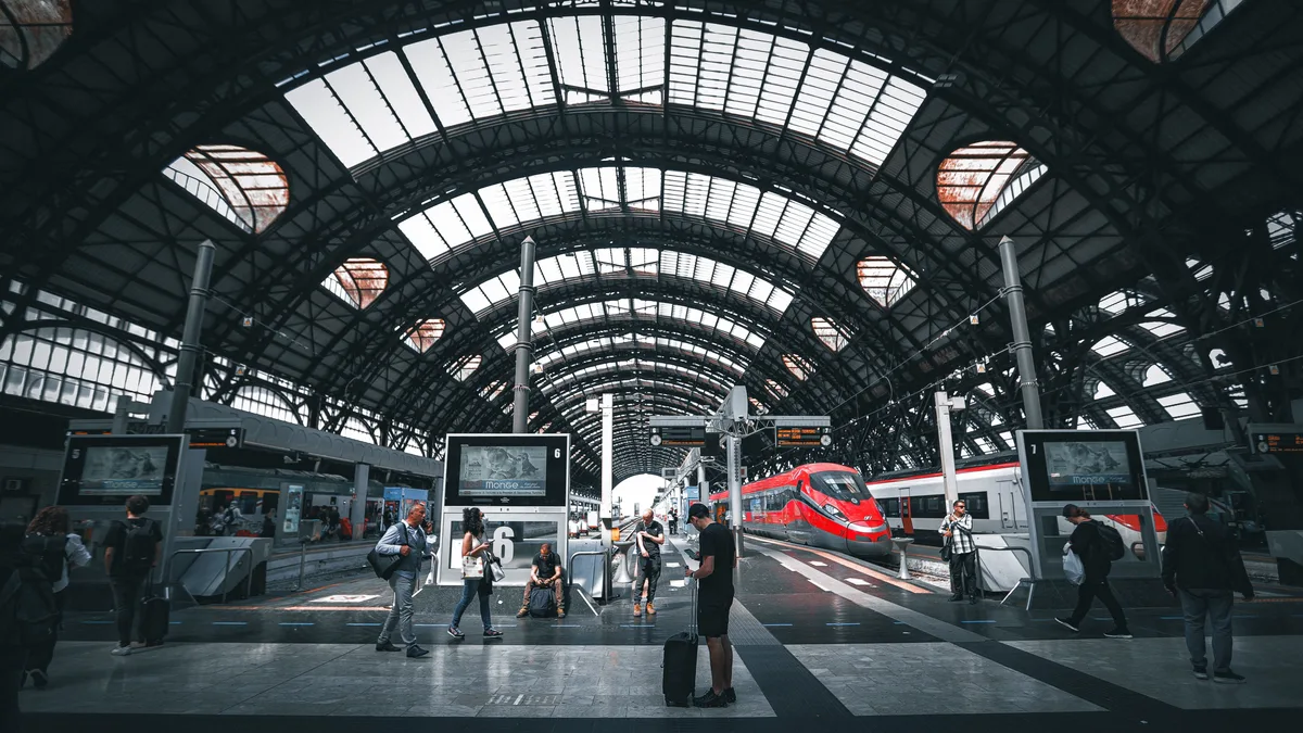 Pendler am Mailänder Hauptbahnhof mit modernen Zügen unter dem ikonischen gewölbten Dach.