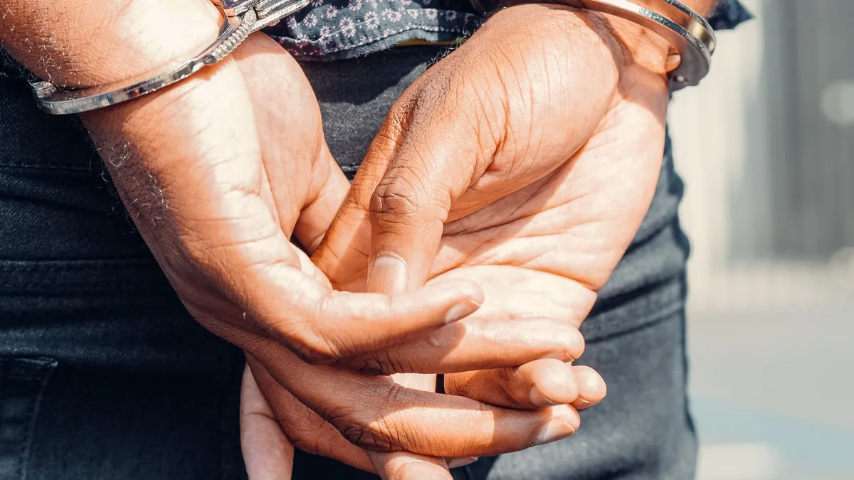 Rückansicht einer Person in Handschellen im Freien, die Rechtspflege und Gerechtigkeit symbolisiert.
