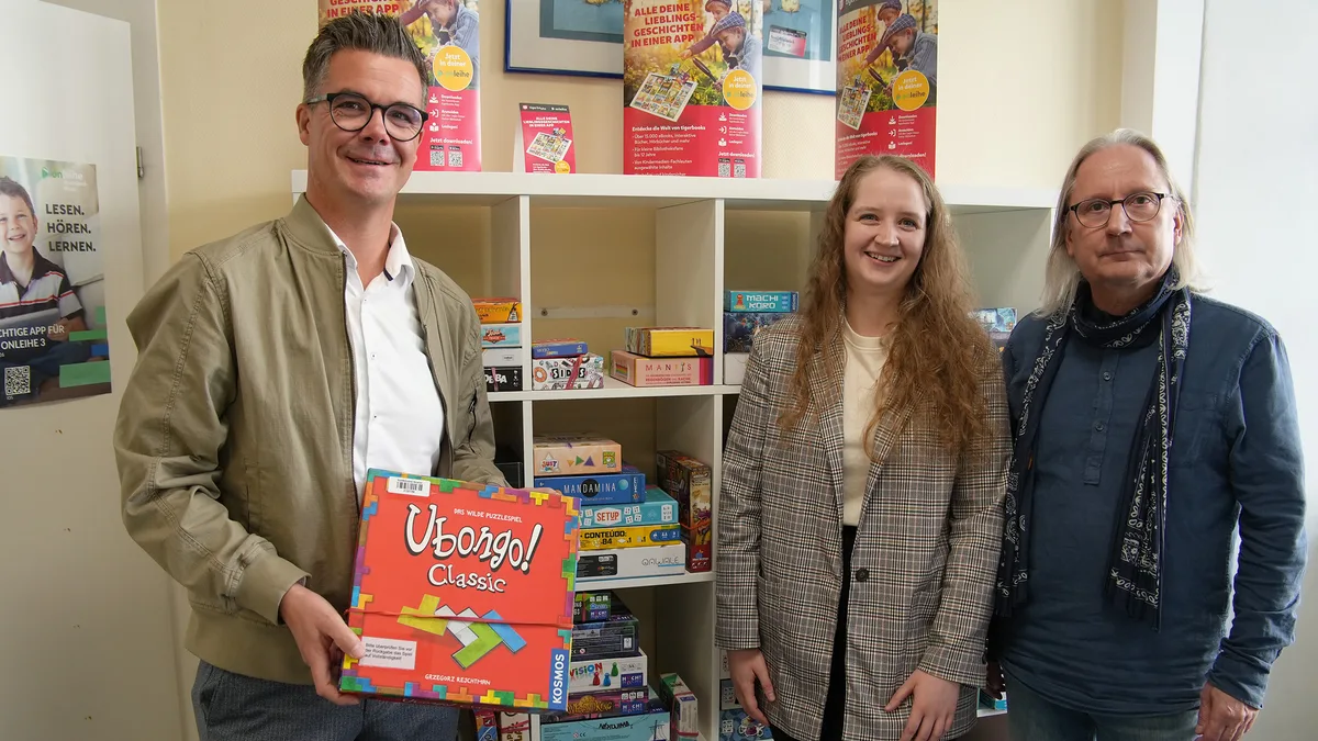 Bürgermeister Peter Jung und die Bibliotheksleitung Anna Lenz und Volker Trümper stöbern in der Stadtbibliothek Neuwied nach Gesellschaftsspielen