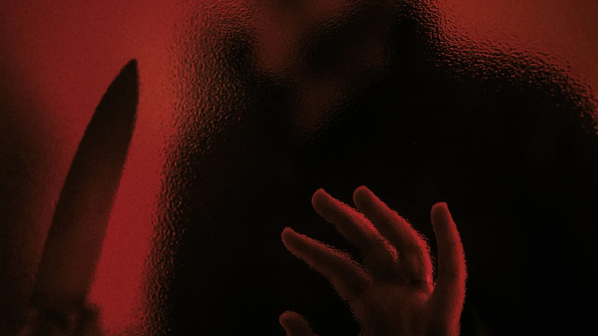Eine schattenhafte Figur mit einem Messer hinter verzerrtem Glas, die eine cineastische Horror-Atmosphäre ausstrahlt.