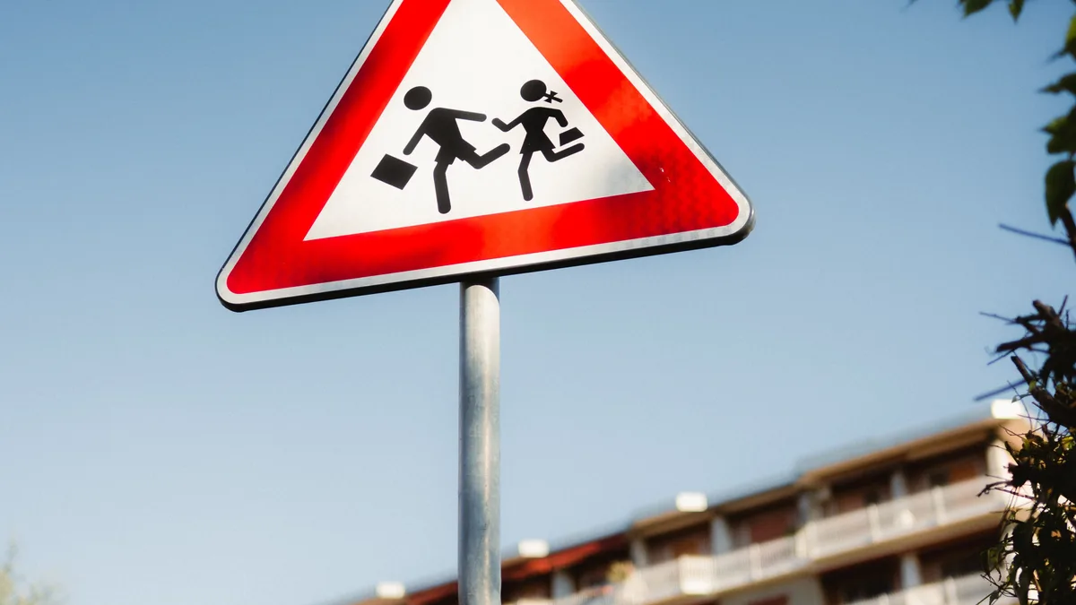 Rotes dreieckiges Warnschild für Schulzone im Stadtgebiet vor klarem blauen Himmel.