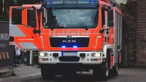 Helles rotes Feuerwehrfahrzeug mit blauen Lichtern auf einer Stadtstraße bei Tageslicht.