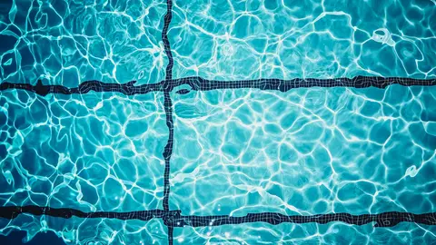 Nahaufnahme einer schimmernden türkisfarbenen Schwimmbadoberfläche mit Fliesenlinien.