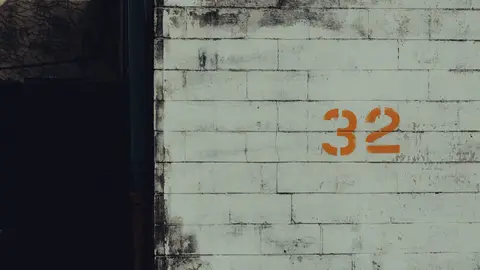 Eine gealterte Stadtmauer mit der Nummer 32 in orangefarbenem Graffiti, die eine raue Stadtlandschaftsästhetik bietet.