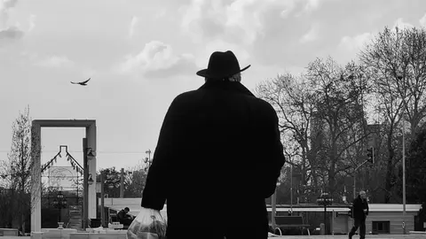 Schwarzweißfoto eines Mannes im Hut, der in einer urbanen Umgebung geht und eine melancholische Stimmung schafft.