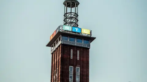 Ikonischer Messeturm in Köln, Deutschland, aufgenommen unter einem klaren blauen Himmel mit Baumästen.