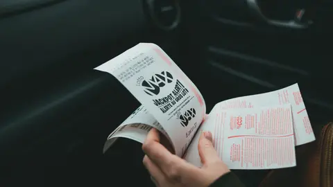 Nahaufnahme von Händen, die Lotto Max-Papiere im Auto halten, was Glück und Zufall symbolisiert.
