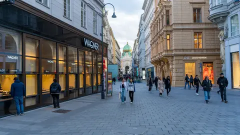 Fußgänger, die in der historischen Altstadt von Wien spazieren, mit ikonischer Architektur und Luxusgeschäften.