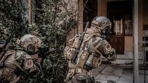 Zwei Soldaten in Tarnung nähern sich mit Gewehren während einer urbanen Militärmission.