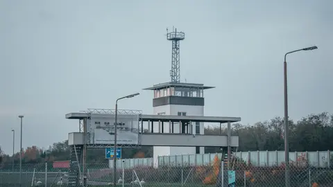 Ein moderner Kontrollturm an einem Flughafen, umgeben von Zäunen und Straßenlaternen.
