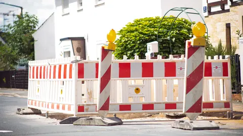 Helle Straßenbarriere mit gestreiftem Muster signalisiert Bauarbeiten in einer Vorstadtstraße.
