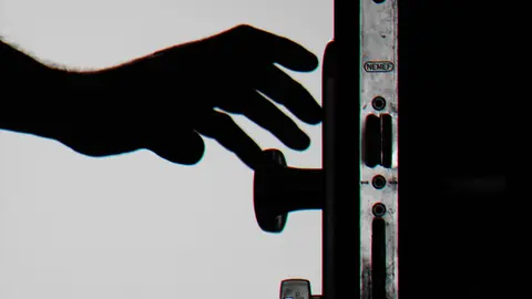 Silhouette einer Hand, die kurz davor steht, eine Tür mit Schlüsseln im Schloss zu öffnen, symbolisiert Sicherheit.