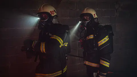 Feuerwehrleute in vollständiger Ausrüstung, die unter dunklen Bedingungen mit Taschenlampen arbeiten.