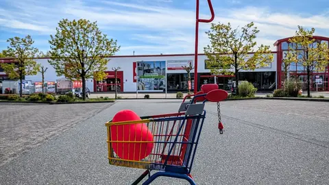 Bunter Einkaufswagen mit rotem Ball im Freien auf einem leeren Parkplatz unter klarem Himmel.