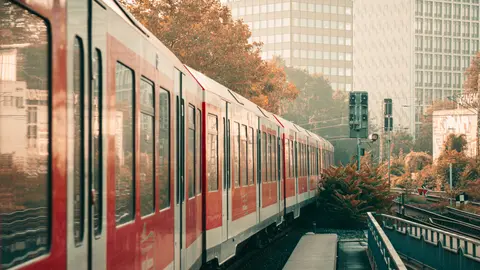 Roter Zug auf erhöhten Gleisen in Hamburg mit Gebäuden und Herbstlaub.