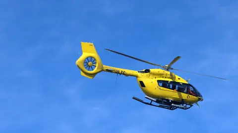 Ein leuchtend gelber Hubschrauber im Flug vor klarem, blauem Himmel.