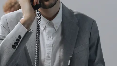 Fokussierter junger Mann in einem grauen Anzug, der am Schreibtisch im Büro telefoniert.