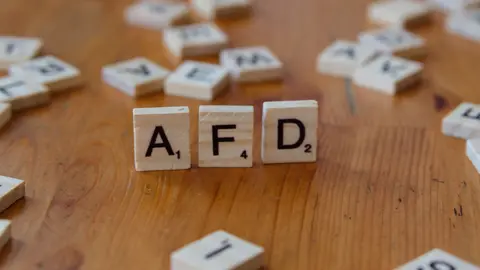 Nahaufnahme von Scrabble-Steinen mit dem Wort „AFD“ auf einer Holztischoberfläche, die politische Konzepte symbolisieren.
