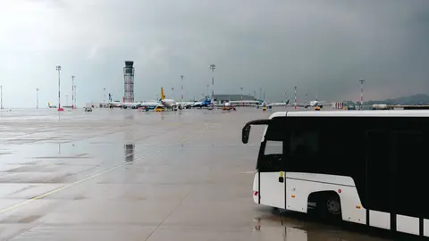 Verregnetes Flughafenrollfeld mit einem Passagierbus und Flugzeugen im Hintergrund.