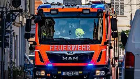 Ein leuchtendes Feuerwehrauto mit der Aufschrift „Feuerwehr“ fährt durch eine Berliner Straße und reagiert auf einen Notfall.