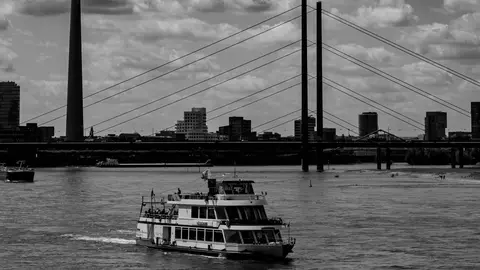 Schwarzweißbild der Skyline von Düsseldorf mit einem Boot auf dem Rhein, das berühmte Sehenswürdigkeiten zeigt.