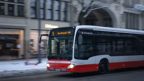 Ein rot-weißer Linienbus fährt durch die verschneiten Straßen in Hamburg mit Feiertagsdekorationen.