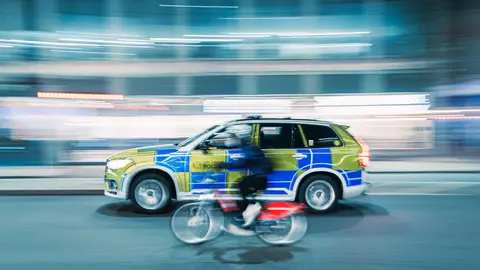 Dynamischer Bewegungsunschärfe-Schuss eines Radfahrers und eines Polizeiautos auf einer Stadtstraße bei Nacht.