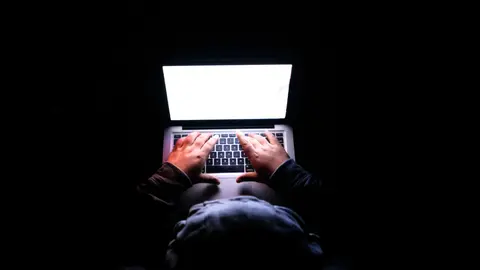 Eine Person in einem dunklen Raum, die auf einem Laptop tippt, was Privatsphäre, Cybersicherheit und Technologie symbolisiert.