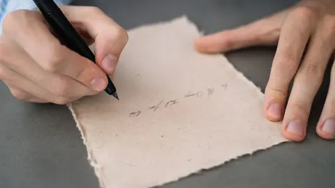 Hände, die in Kalligraphie auf rustikalem Pergamentpapier schreiben. Perfekt für Vintage- oder künstlerische Themen.
