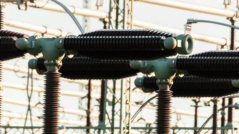 Nahaufnahme von elektrischen Energieanlagen im Freien mit Isolatoren und Leitern.