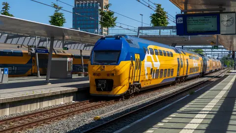 Bunter blauer und gelber Zug, der an einem sonnigen Tag am Utrecht Hauptbahnhof in den Niederlanden ankommt.
